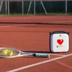 Lifepak CR2 Defibrillator on a tennis court next to a ball and racquet