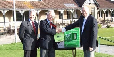 Three men posing next to AED for a photo