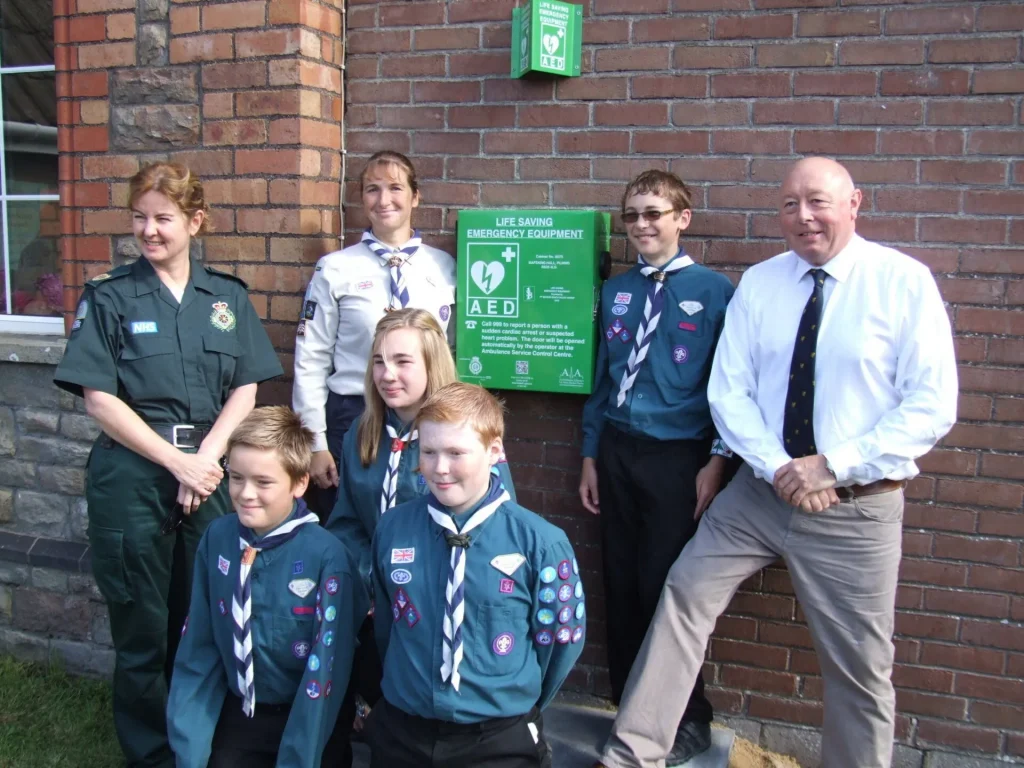 Group Of Scouts Stood around HeartSafe Defibrillator On Wall